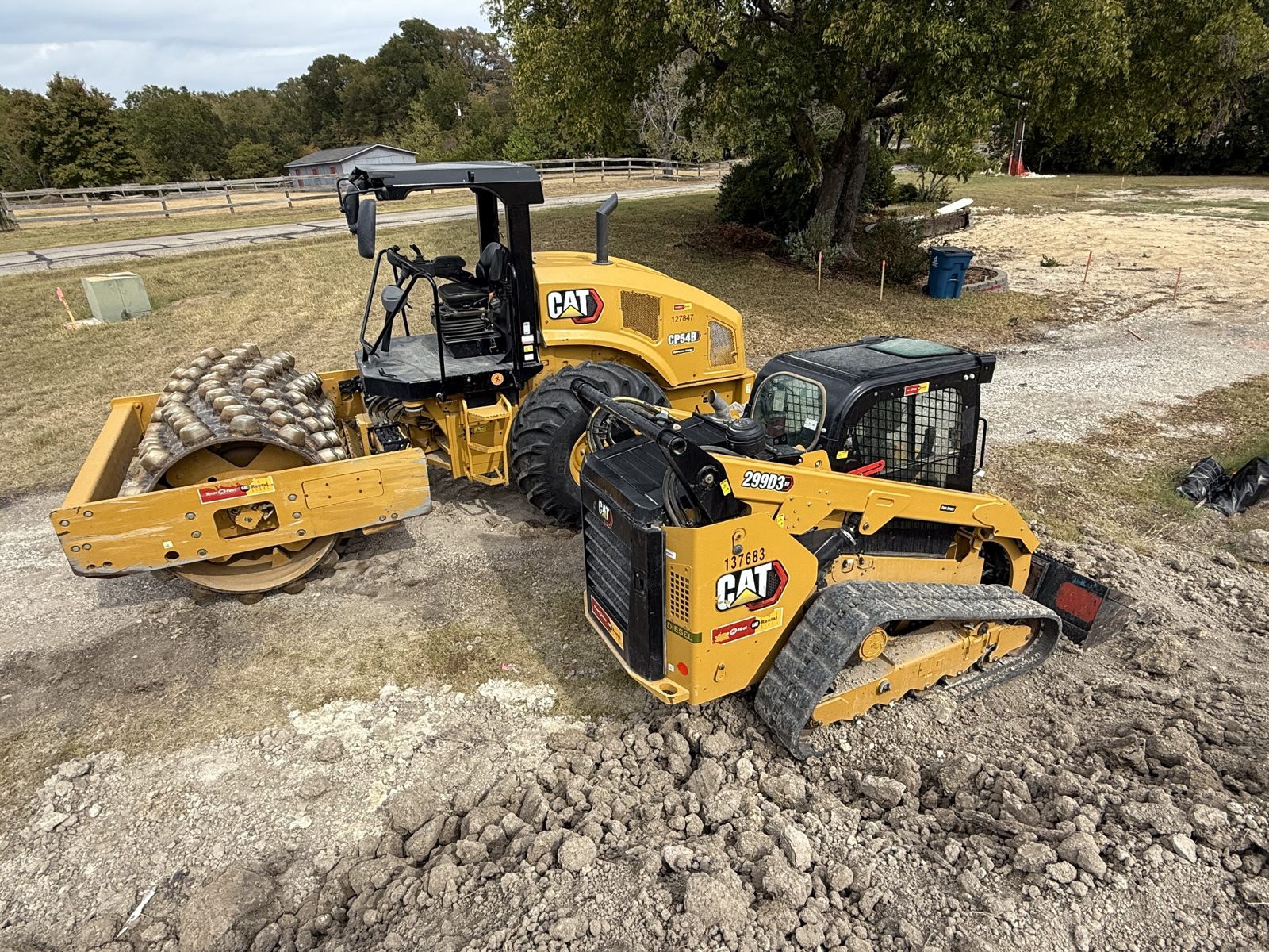 Roller and skid steer staged on a finished dirt pad at the end of a working day