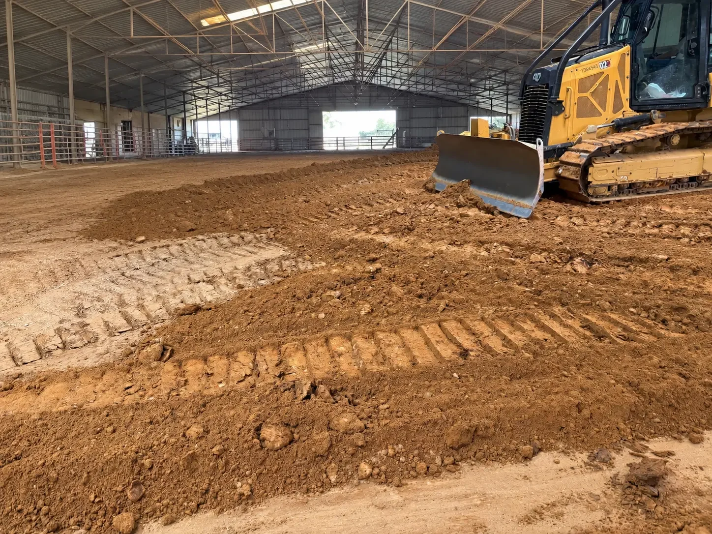 Track dozer grading fresh sandy footing inside a covered horse arena in Pilot Point, Texas