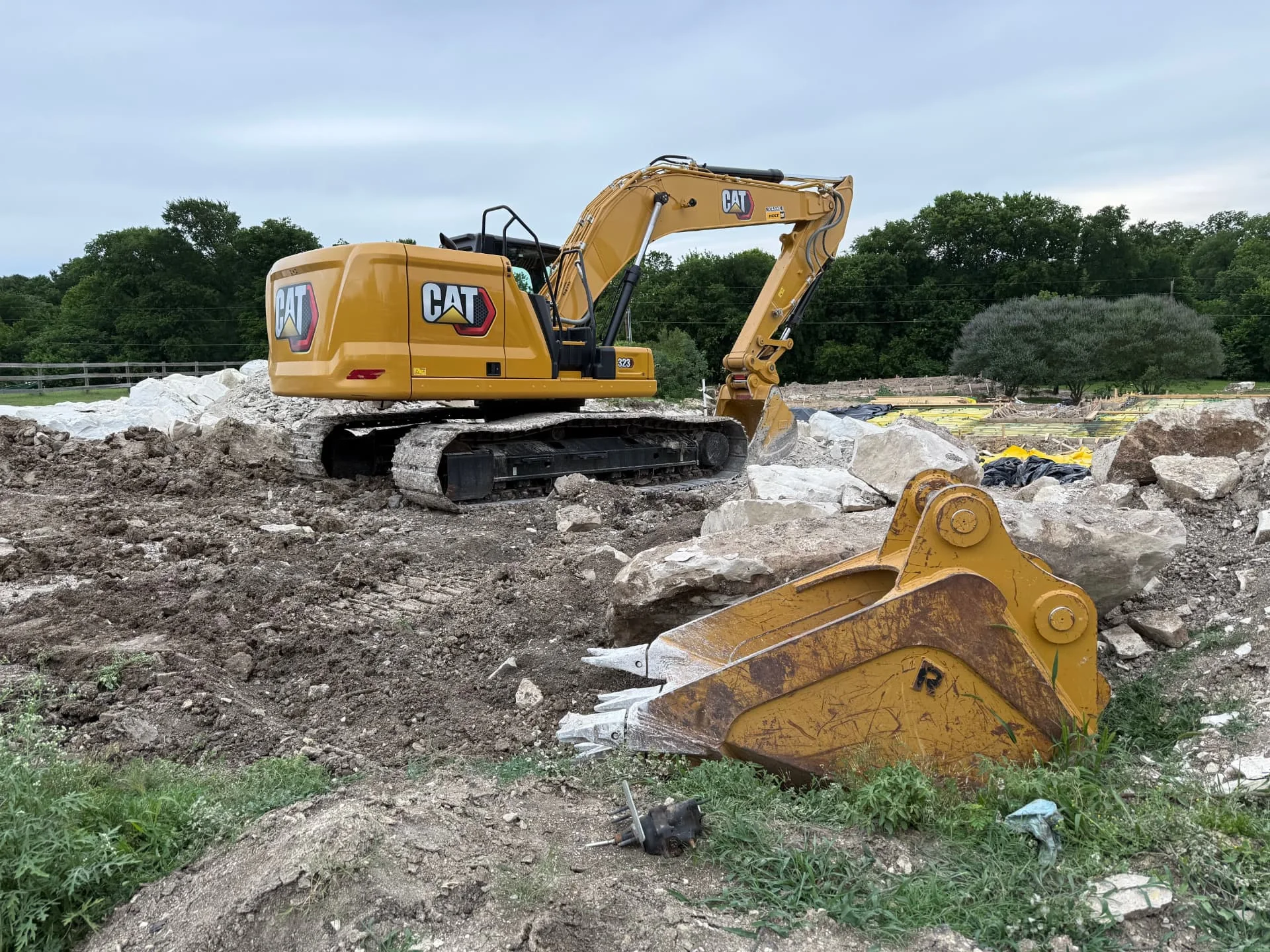 Excavator with a rock bucket breaking out limestone beside a new home foundation