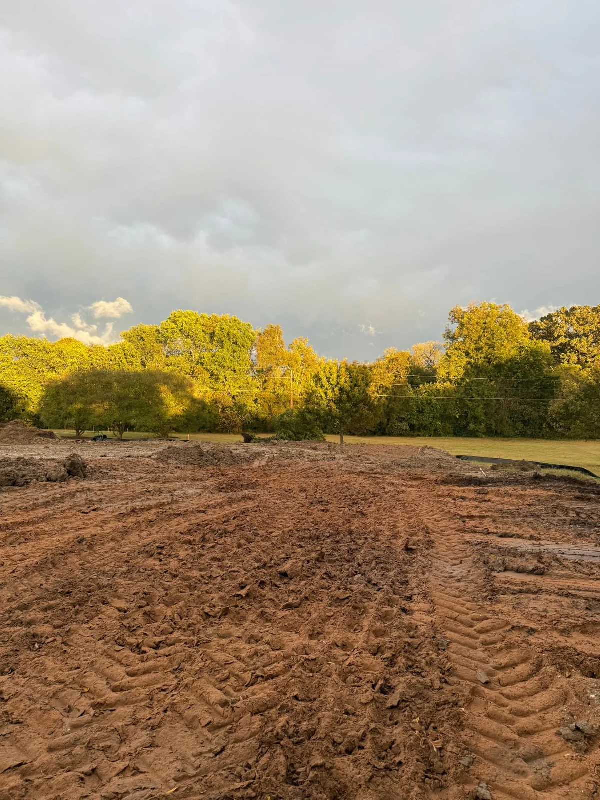 Graded and leveled house pad site with red dirt and tree line in Sherman, Texas