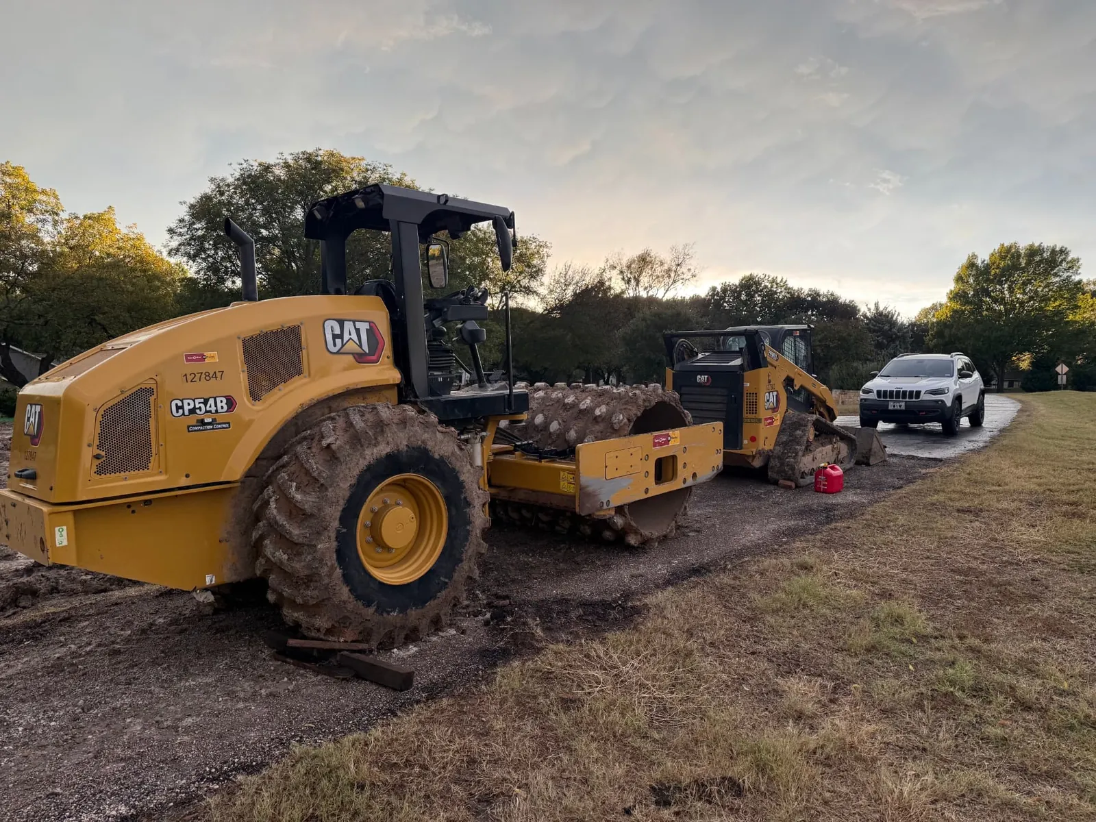 Skid steer placing compacted fill to raise the grade of a driveway run
